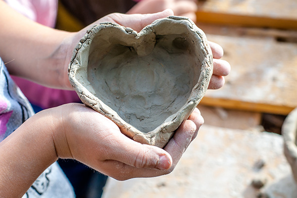 Child makes a heart shaped bowl from clay